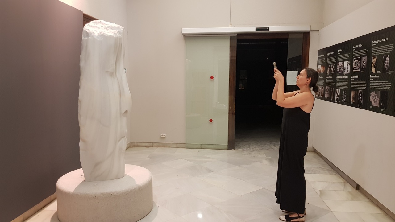 Imagen de una persona fotografiando una escultura de una cara de mármol