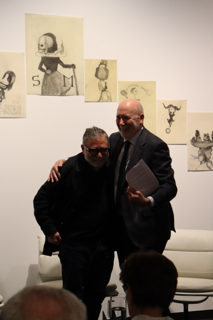 Photograph of two men in front of a wall with drawings smiling at the camera