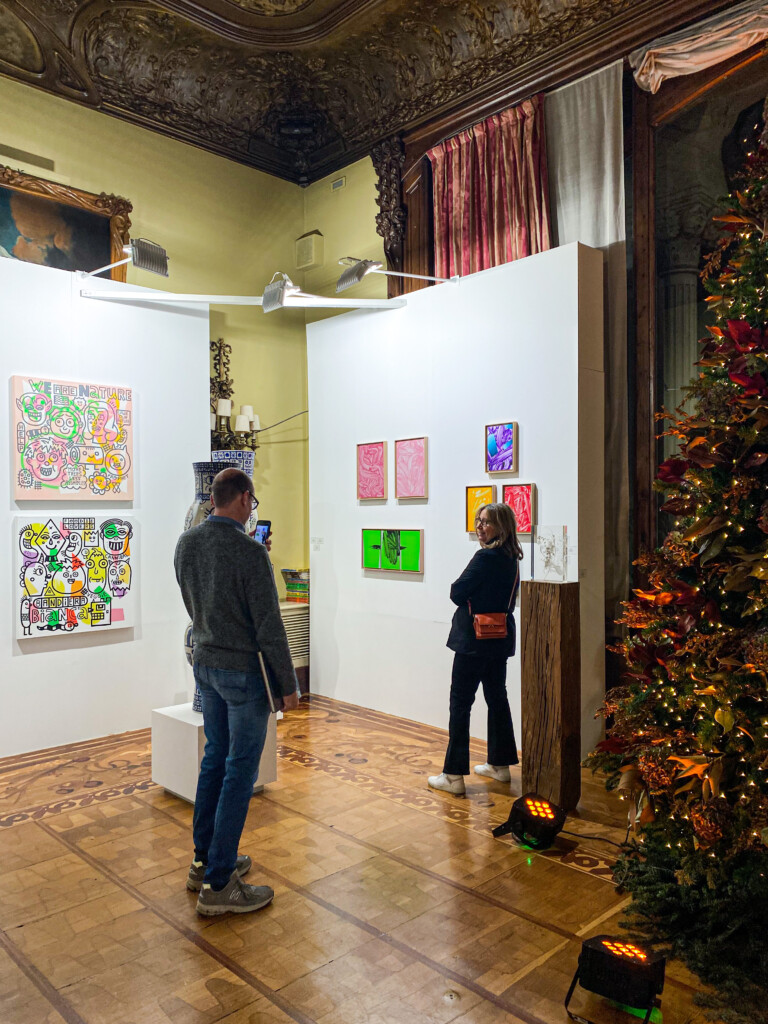 Imagen de una exposición con cuadros coloridos colgados y dos personas observando