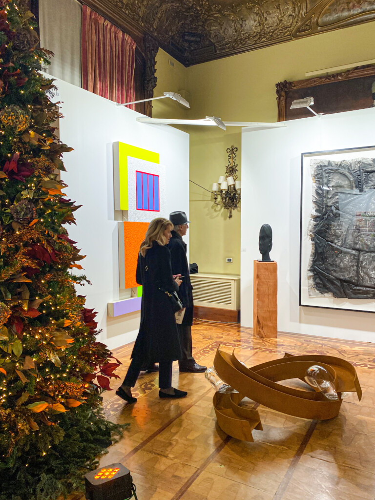 Imagen de una exposición con cuadros y esculturas expuestas y dos personas observando