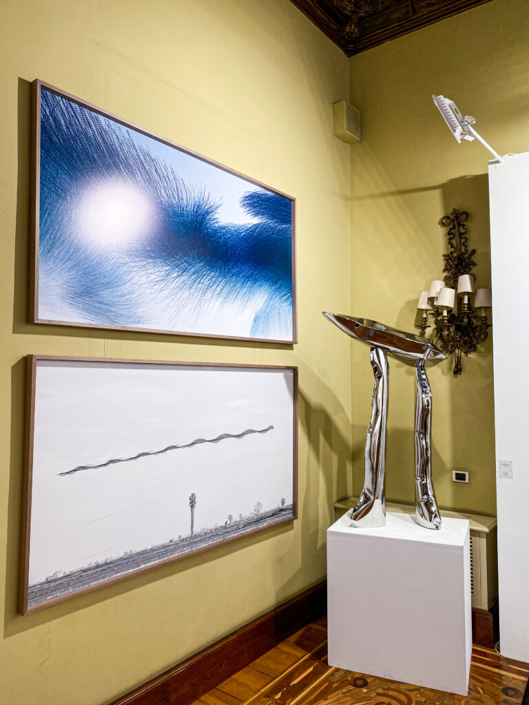 Imatge d'una exposició amb dos quadres, un blau i l'altre blanc, penjats, així com una escultura d'acer inoxidable exposada