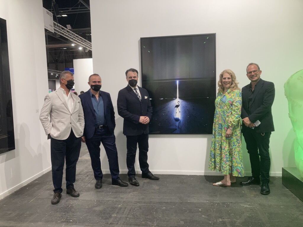 Photograph of four men and a woman smiling at the camera posing in front of a painting