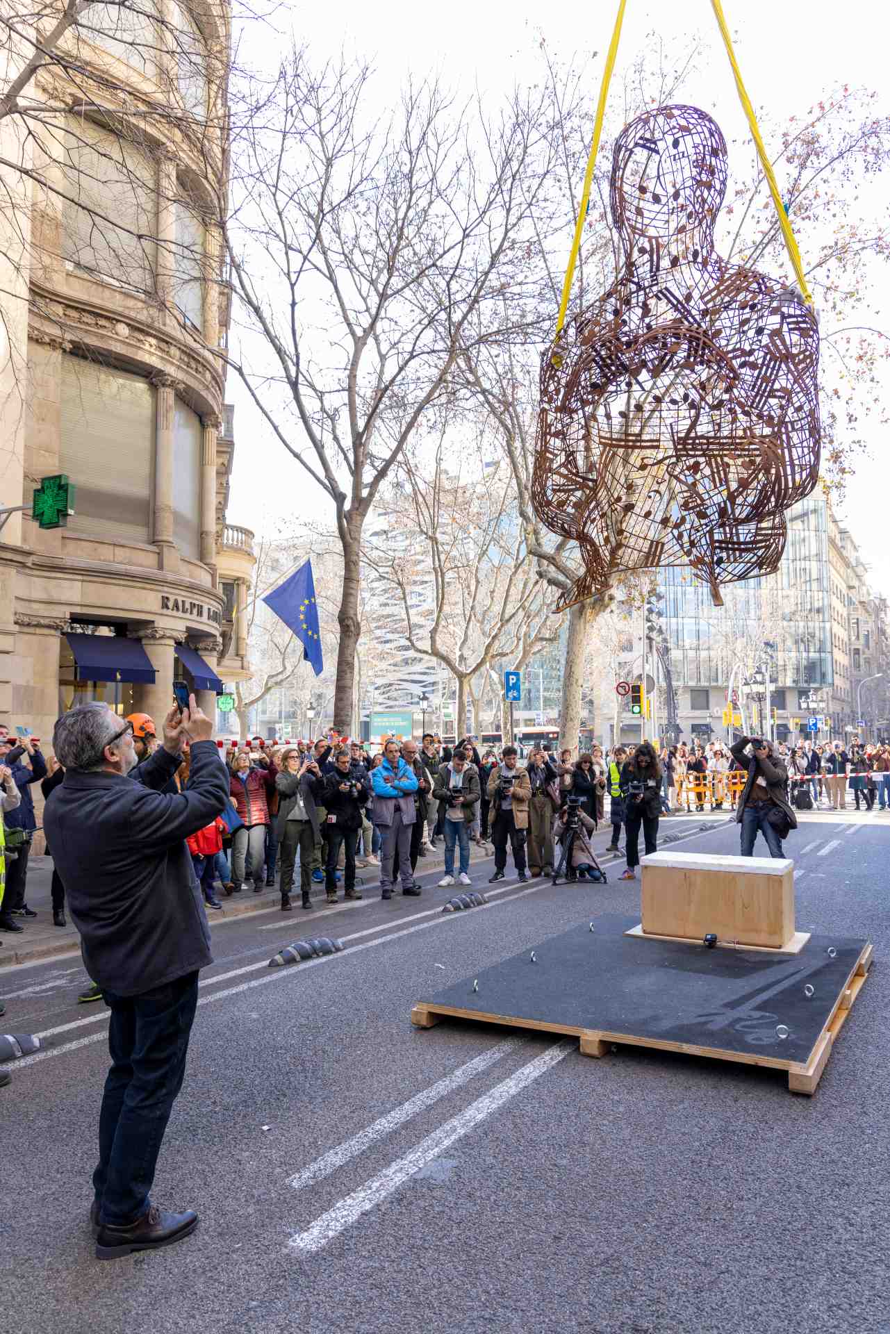 Image of people photographing a metal sculpture picked up by a crane