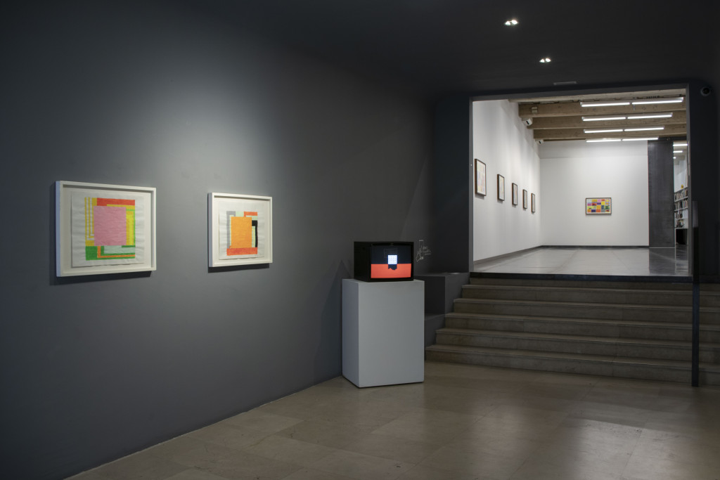Photograph of the entrance of an art gallery with paintings on display and a television playing an animation