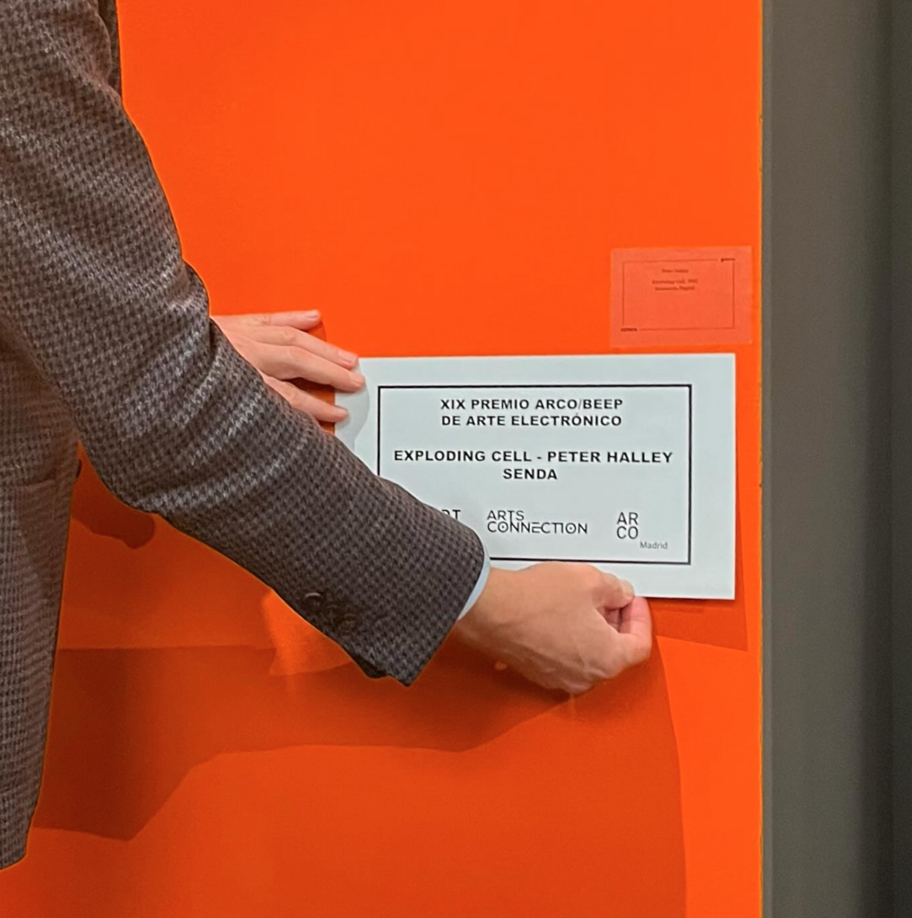 Imatge d'unes mans col·locant un cartell blanc sobre una paret taronja